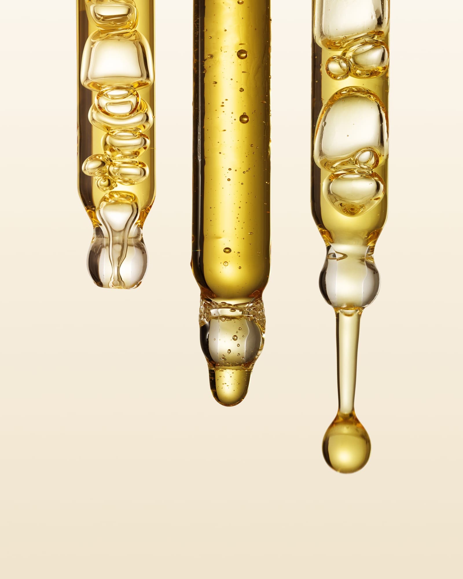 Three glass droppers of golden oil against warm cream